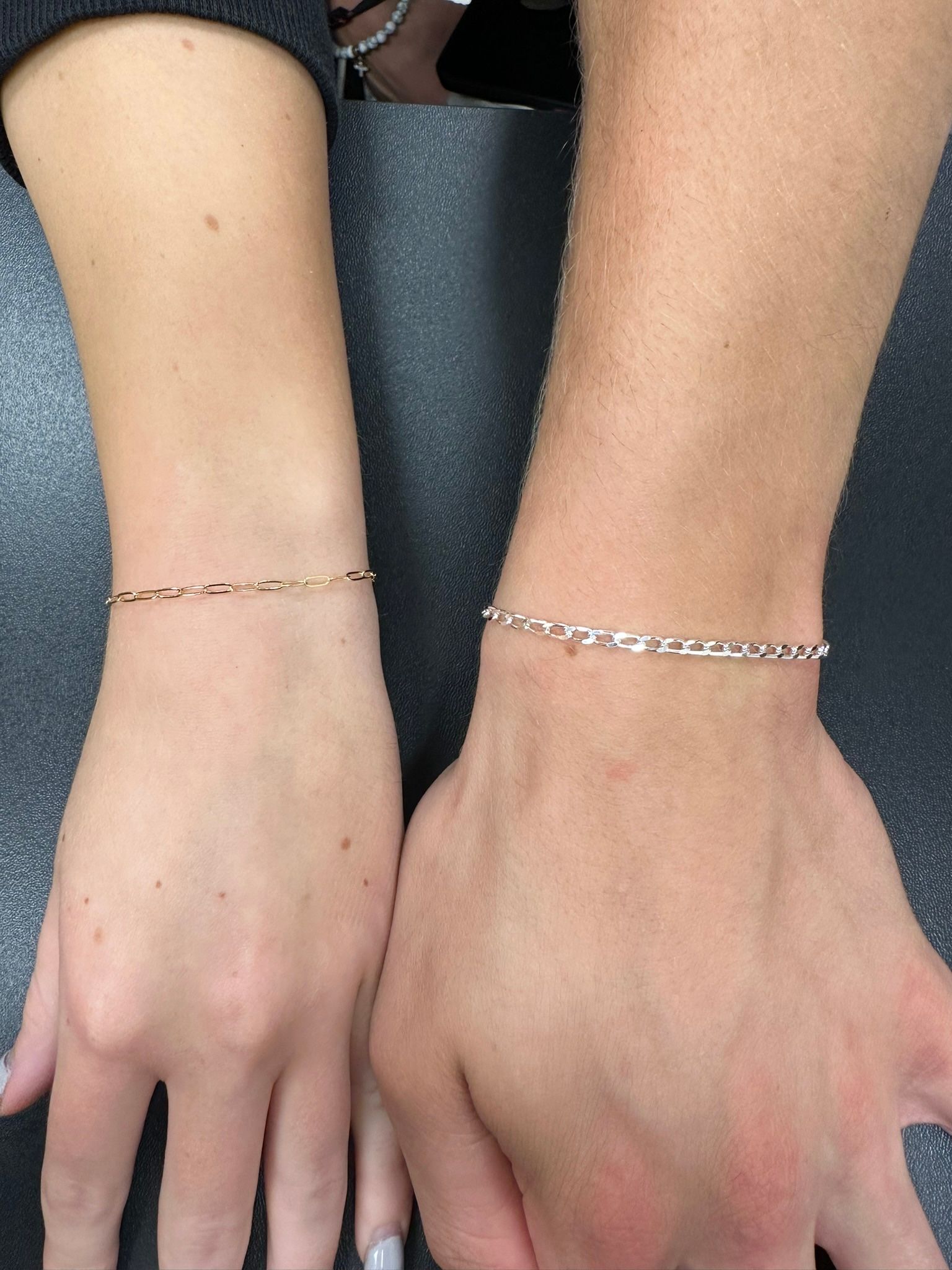 Two wrists with delicate bracelets: one gold, one silver.