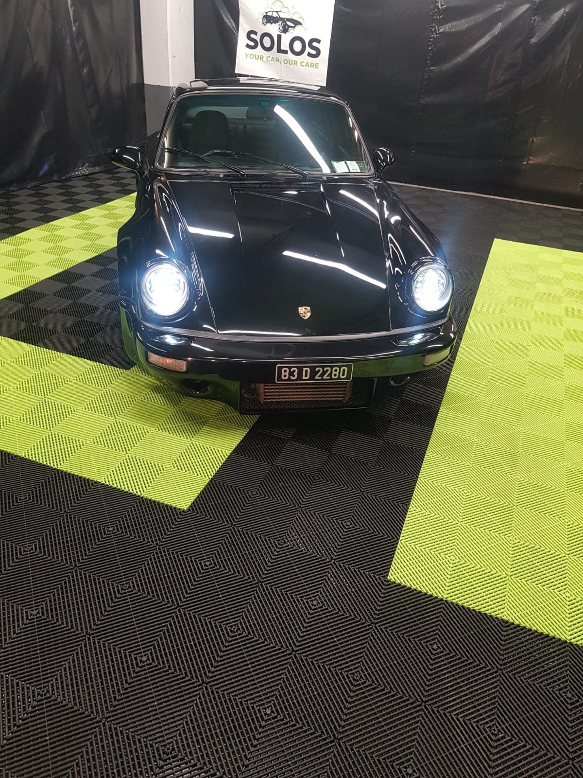 A black porsche is parked on a green and black tile floor.