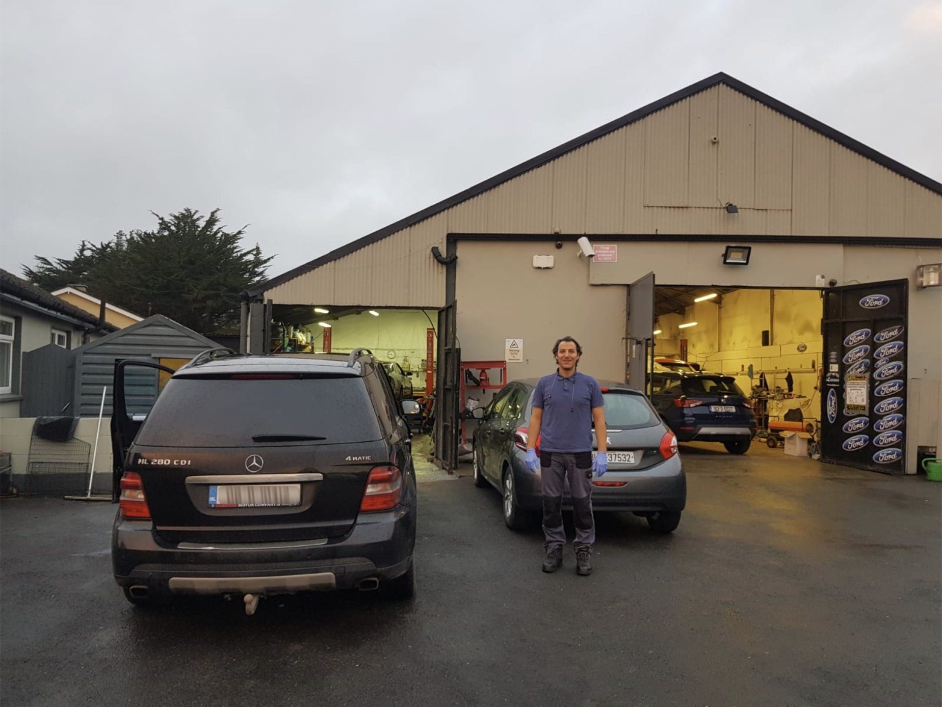A man is standing in front of a garage with cars parked in front of it