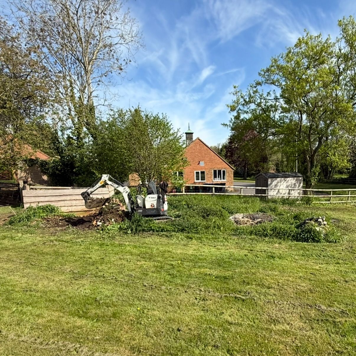 A small excavator is sitting in a grassy field in front of a house.
