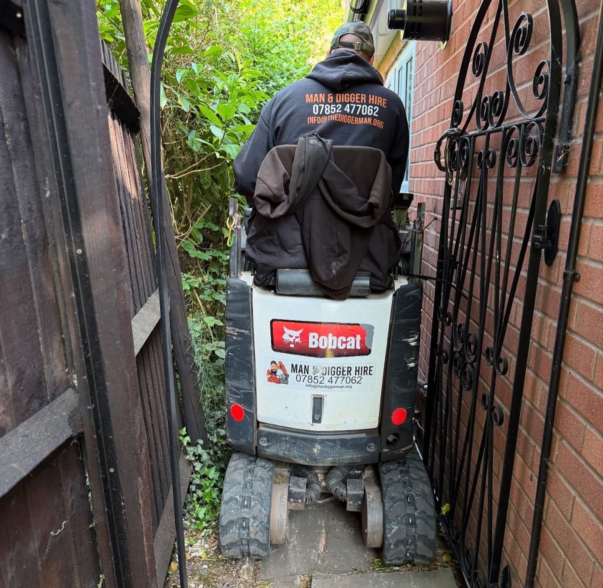 A man is riding a bobcat mini excavator next to a brick wall.