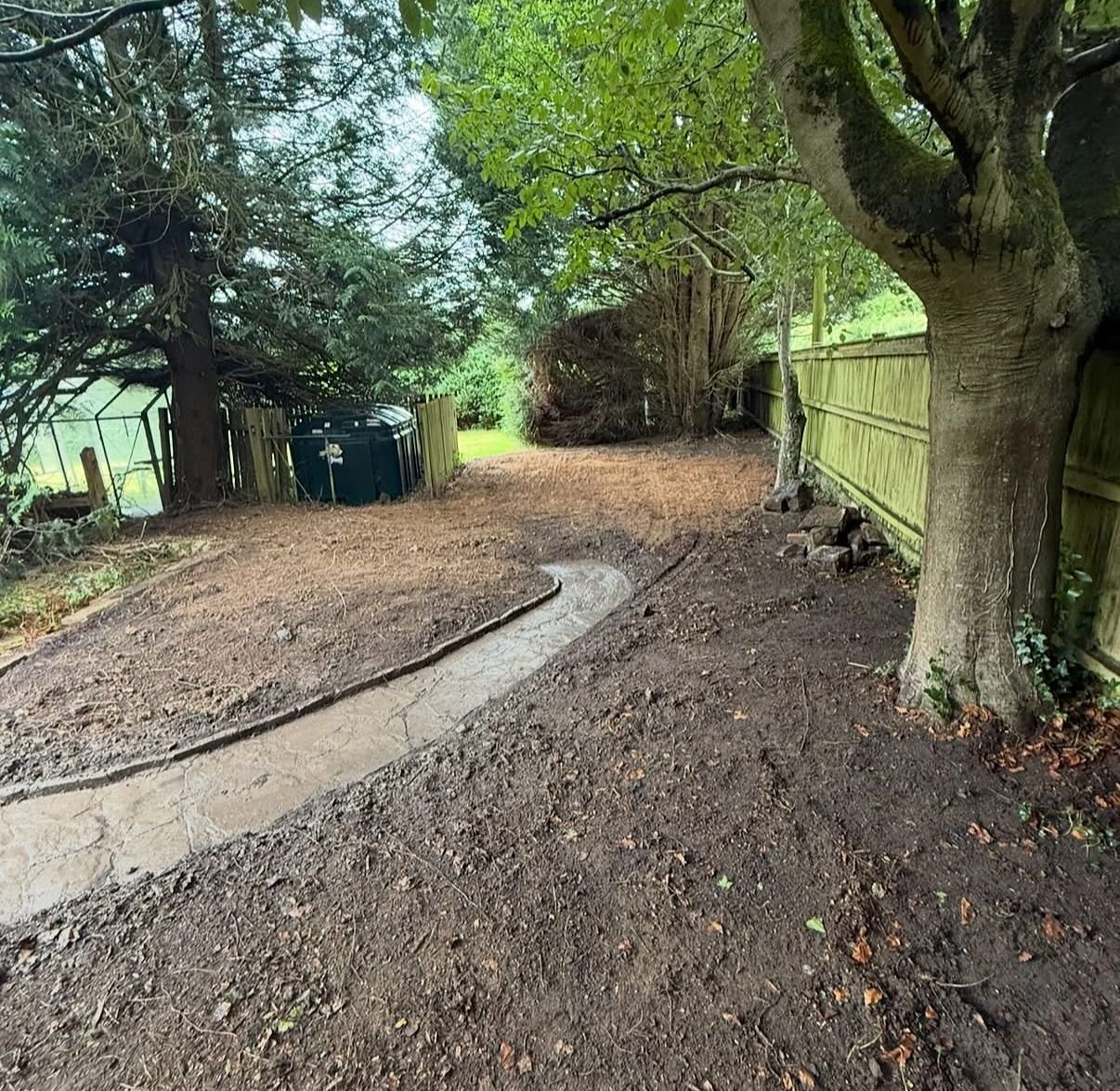 A dirt road with a fence and trees in the background.