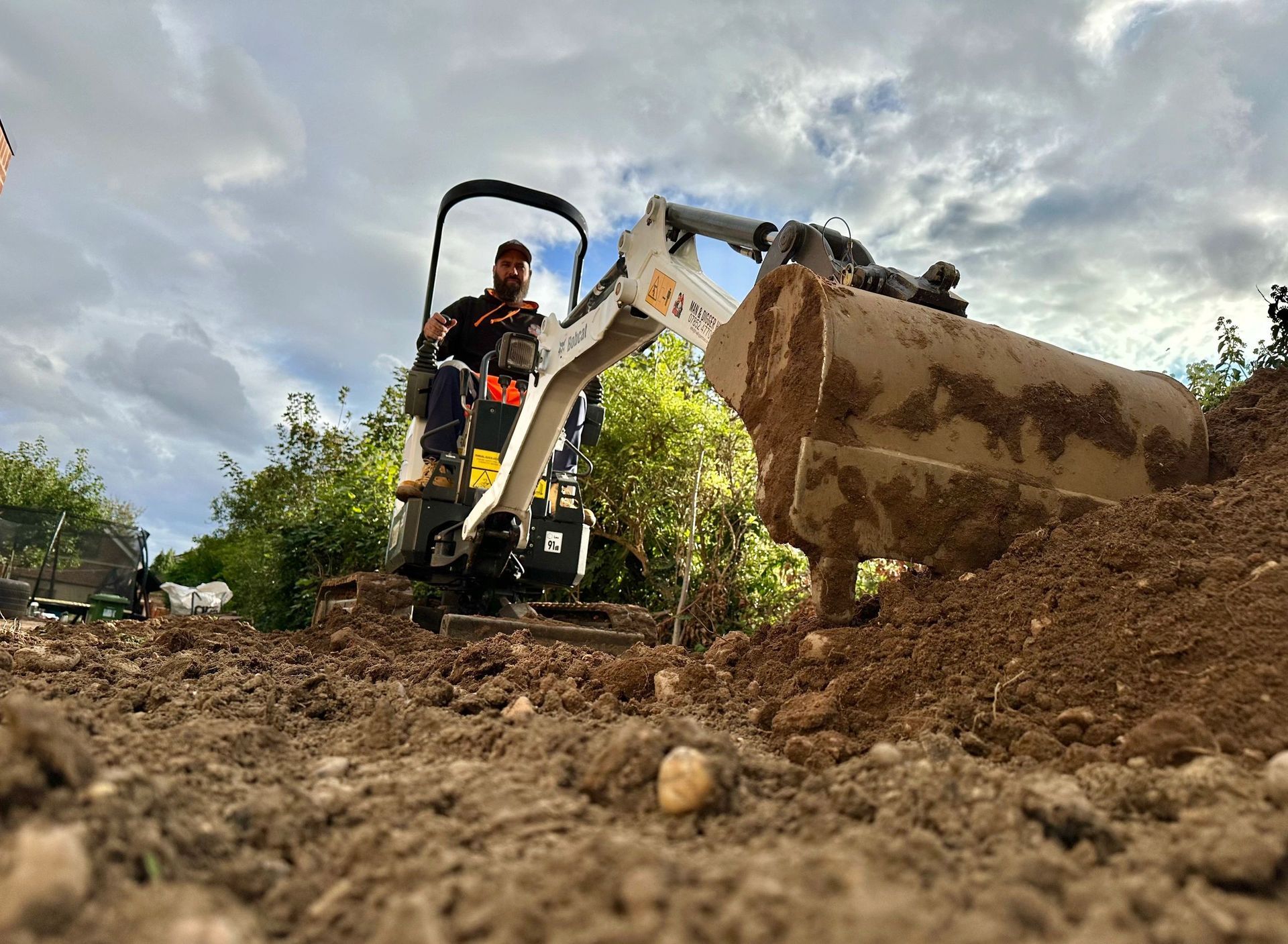 A man is driving a small excavator on a dirt road.