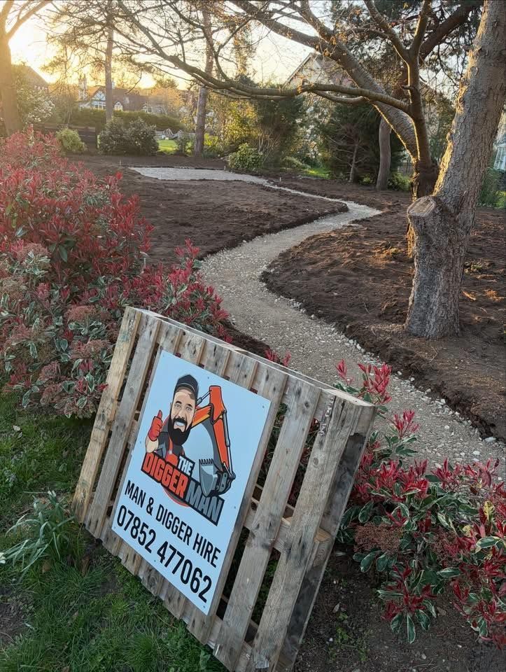 A sign for a digger hire company rests on a wooden pallet in front of a newly excavated garden path at sunset.