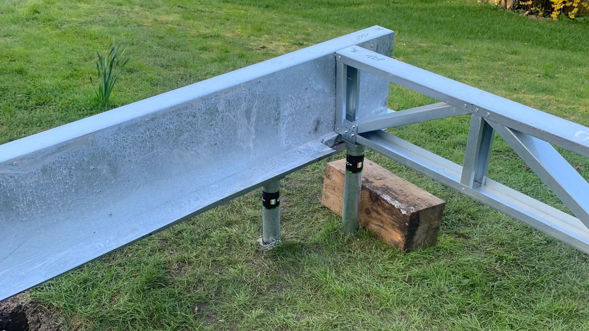 Galvanized steel framework for a deck base supported by metal posts on a grass lawn.