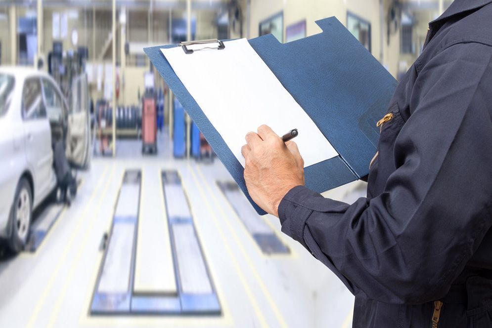 A Mechanic Is Holding A Clipboard And Writing On It In A Garage — SteelBar Restoration In Yarraman, QLD