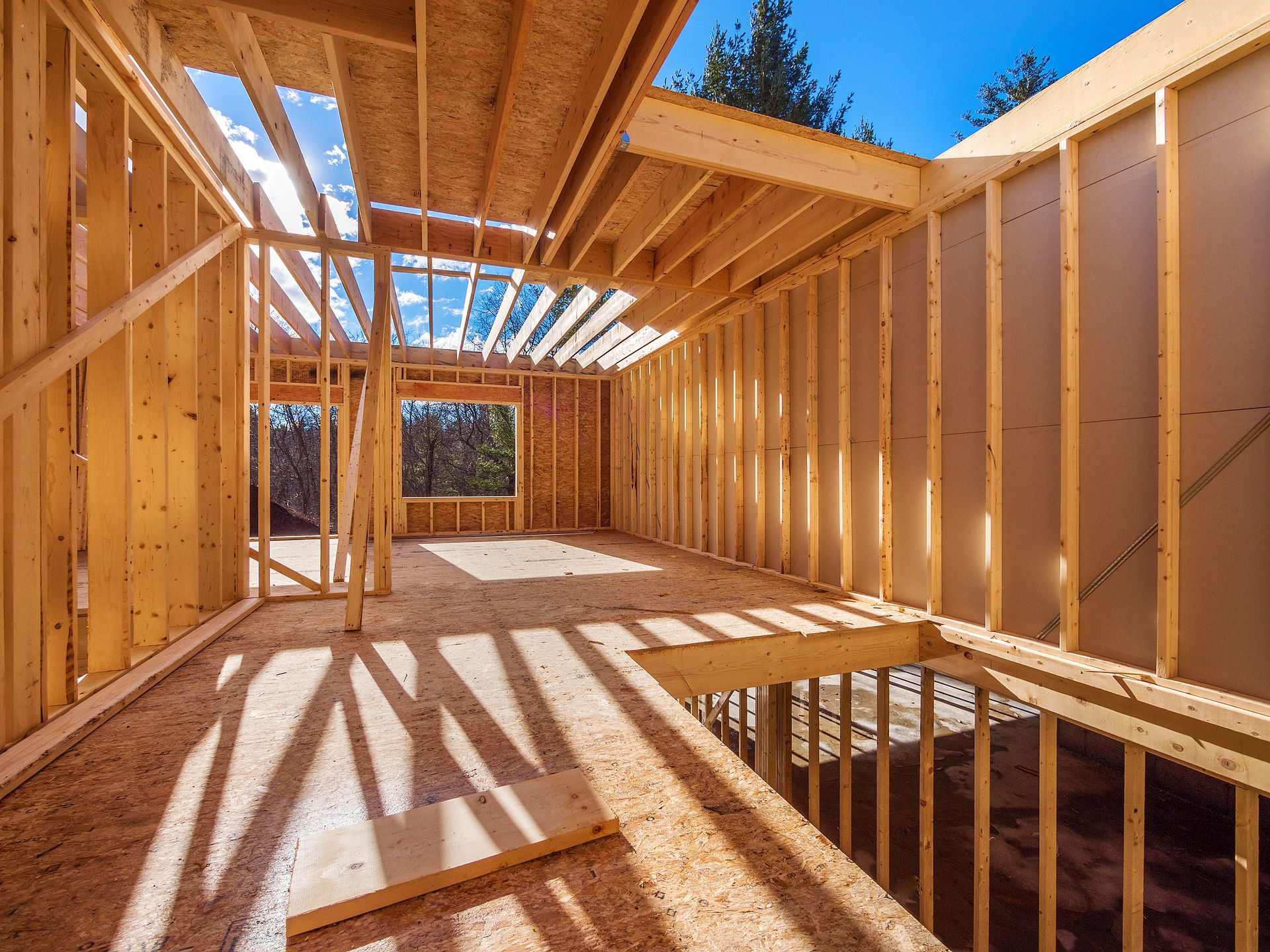 Intérieur d'une maison en construction ; charpente en bois, toit ouvert, lumière du soleil qui entre en rayon.