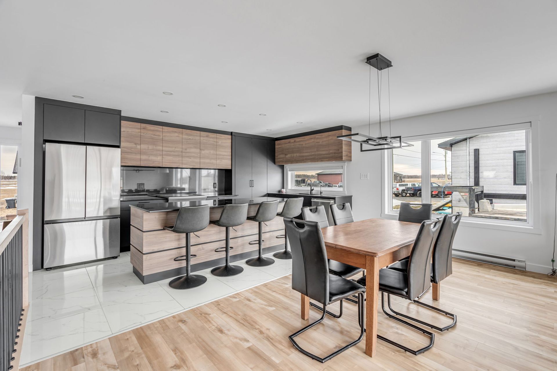 Cuisine moderne avec îlot central et tabourets de bar, table et chaises de salle à manger, et grande fenêtre.