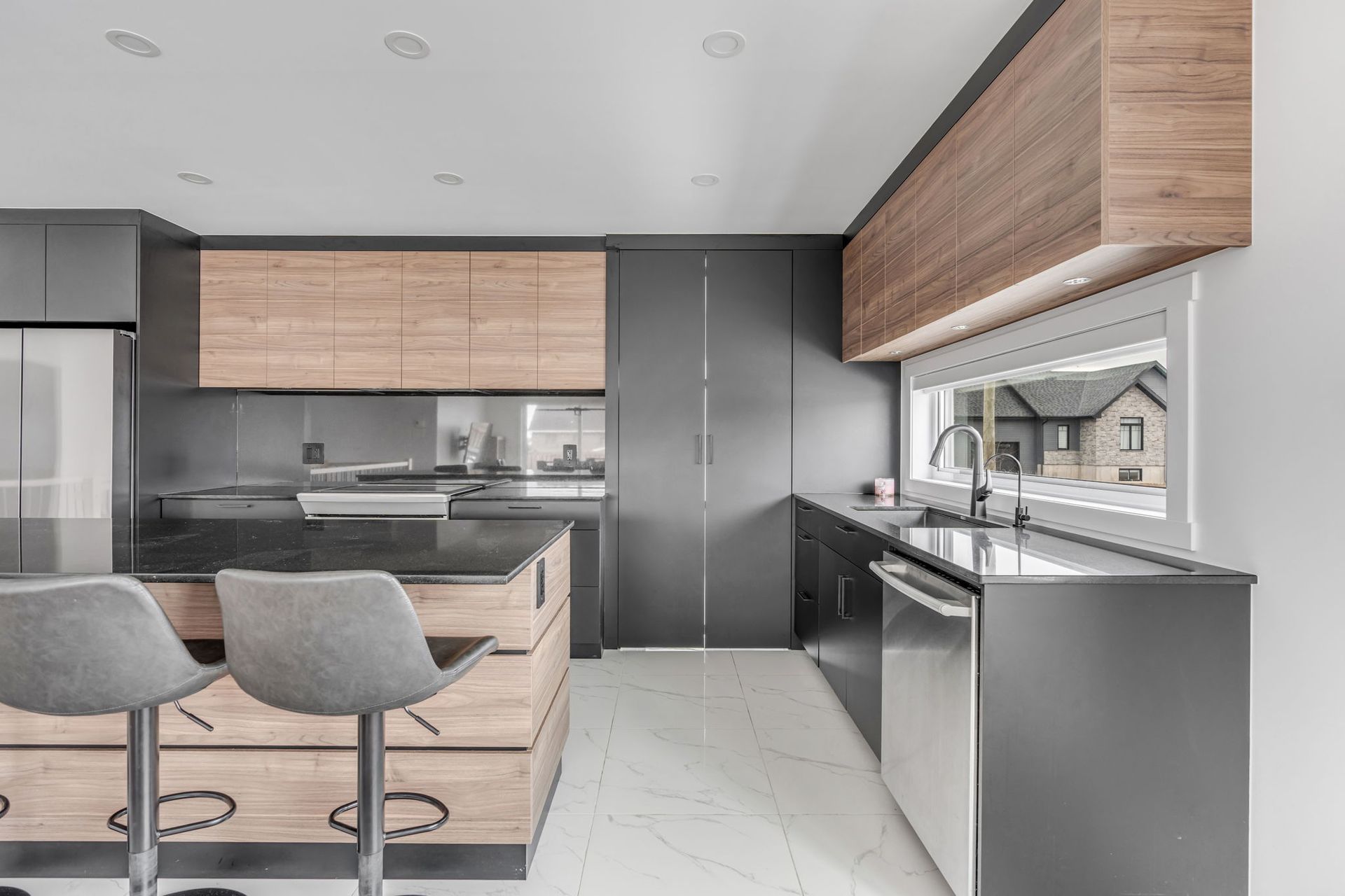 Cuisine moderne avec placards gris foncé, éléments en bois, îlot central avec tabourets de bar et fenêtre.