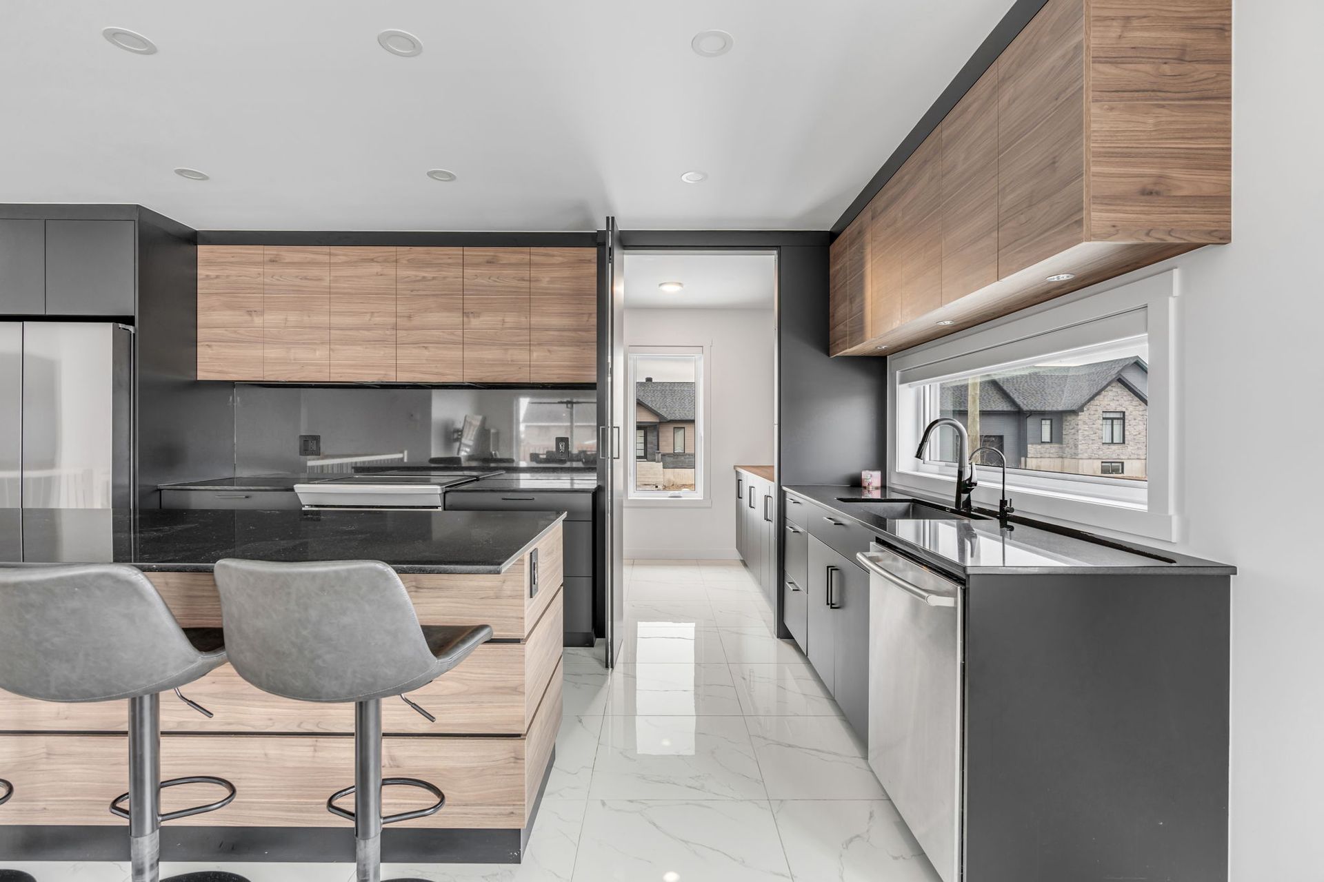 Cuisine moderne avec placards gris et en bois, plans de travail noirs et sol carrelé blanc.