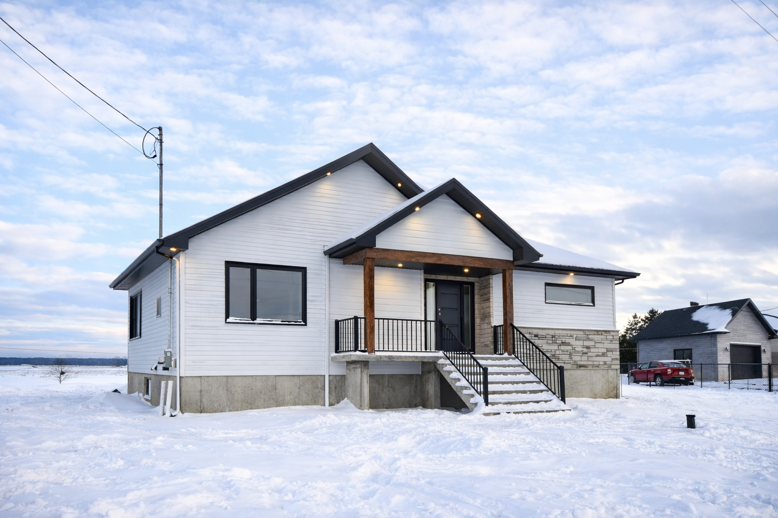 Maison blanche aux boiseries noires, porche en bois, escalier et paysage enneigé.