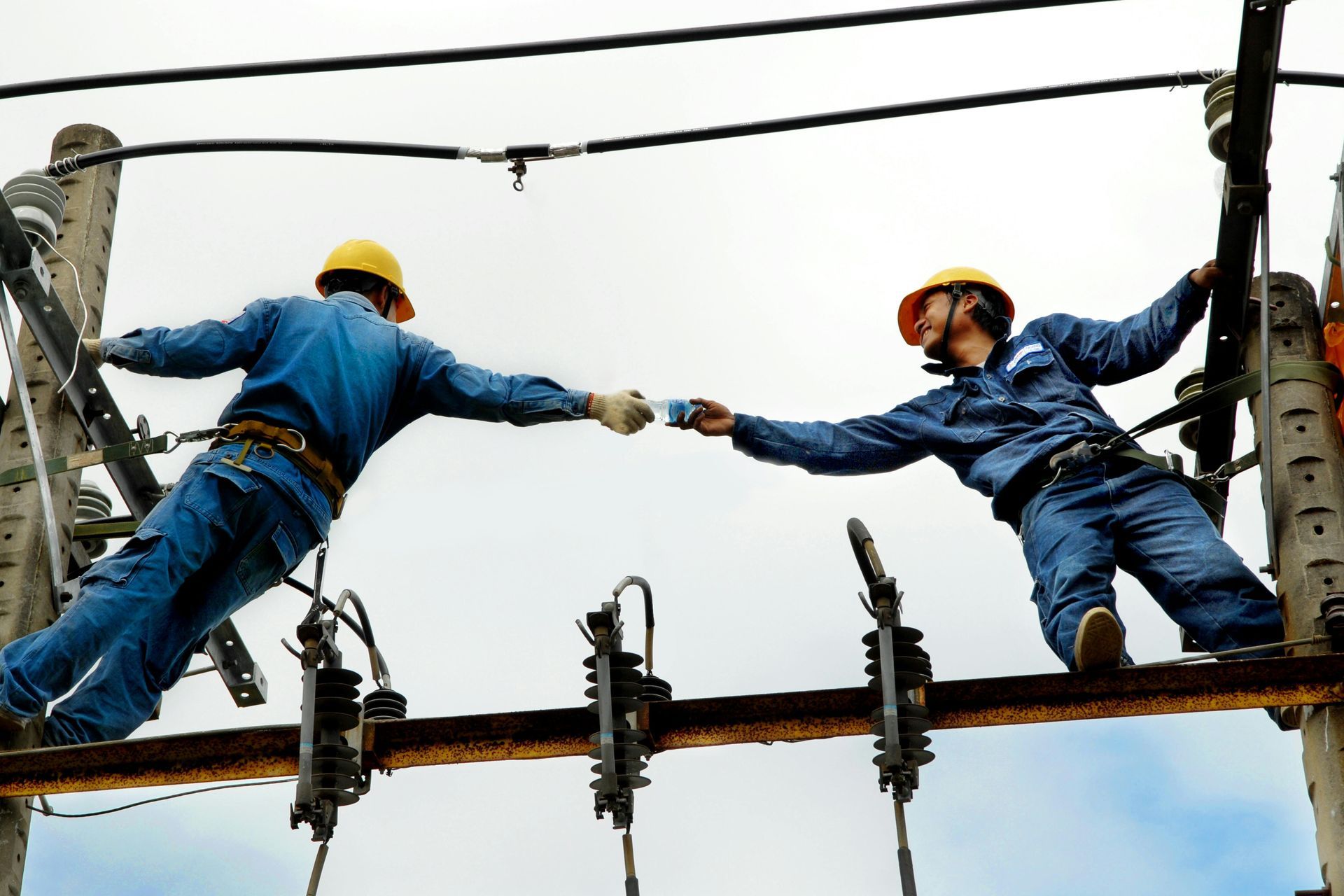 two electricians working side by side and one handing the other water