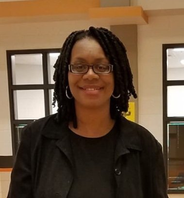 A woman wearing glasses and dreadlocks is smiling for the camera