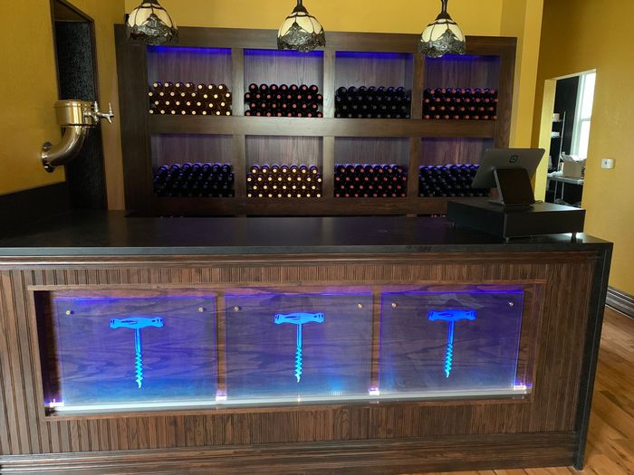 A bar with bottles of wine behind it and the corkscrew logo