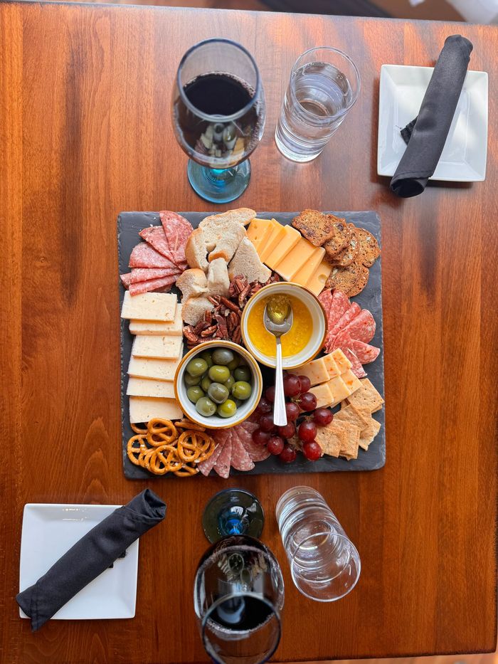 A charcuterie slate filled with meats, cheeses, crackers, grapes, olives, bread, and garlic tapenade.