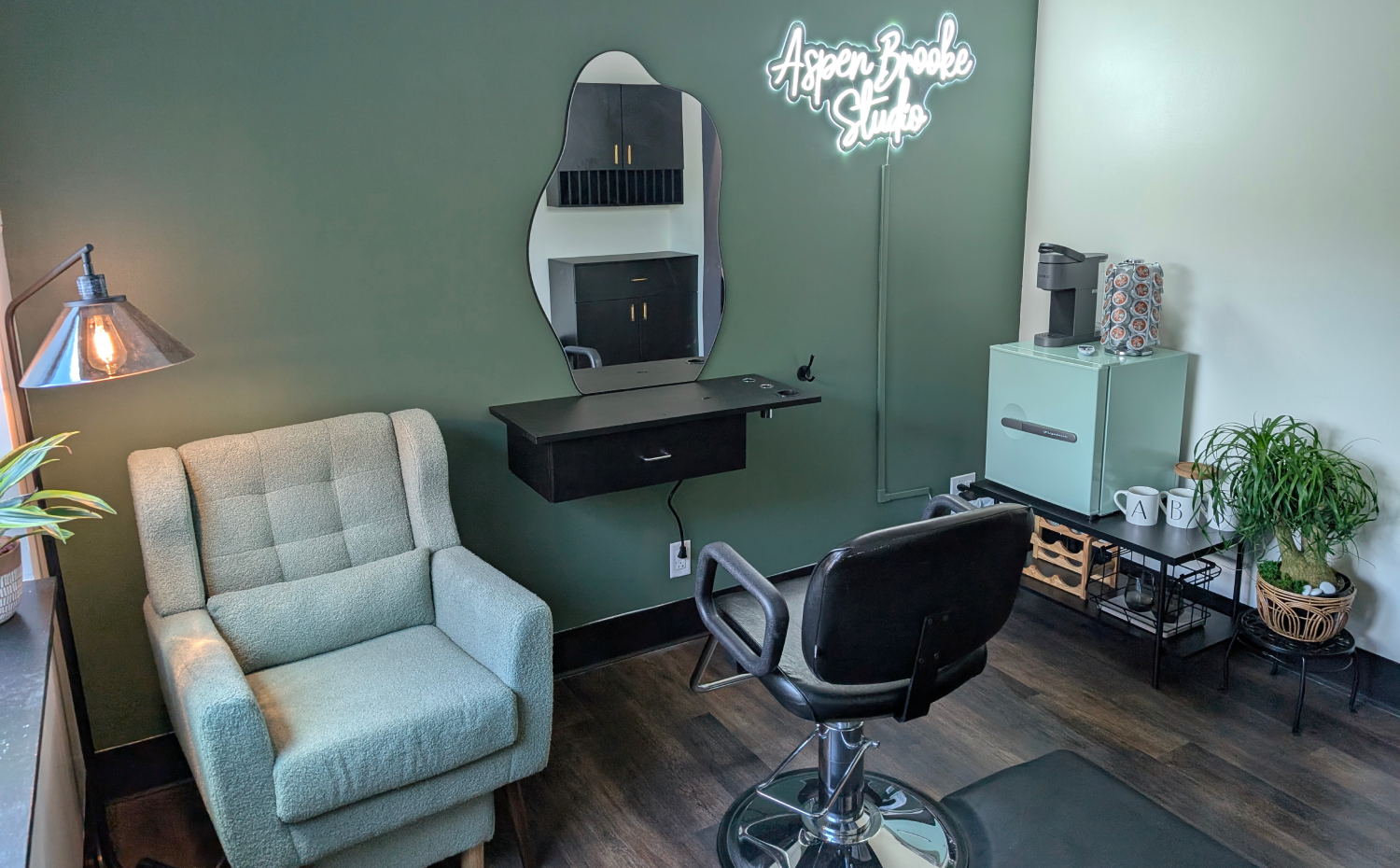 Salon interior with green walls, a mirror, chairs, and a small coffee station.