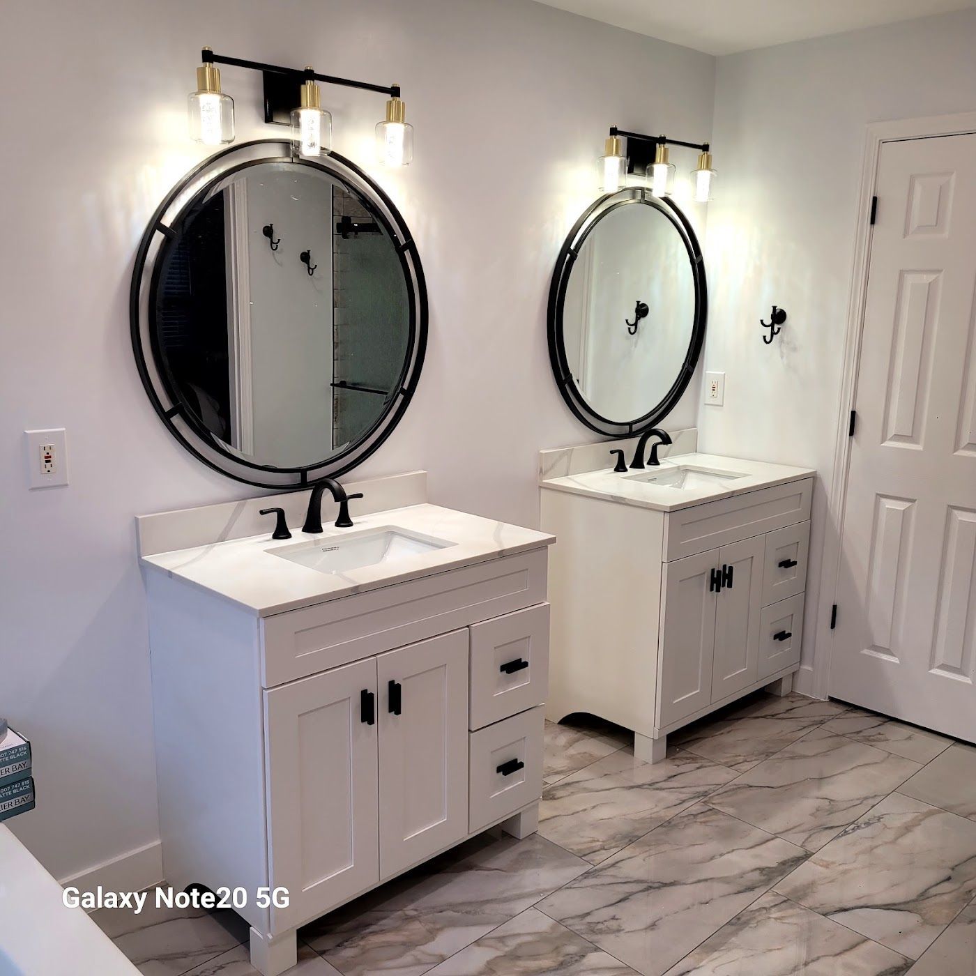 Two white bathroom vanities with black fixtures, round mirrors, and overhead lighting.
