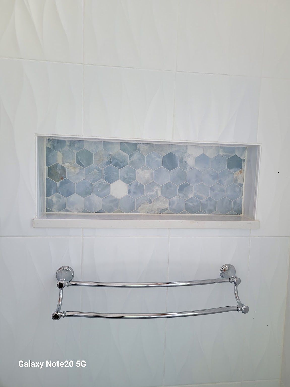 Bathroom wall with recessed shelf of blue hexagon tiles, chrome towel rack below.
