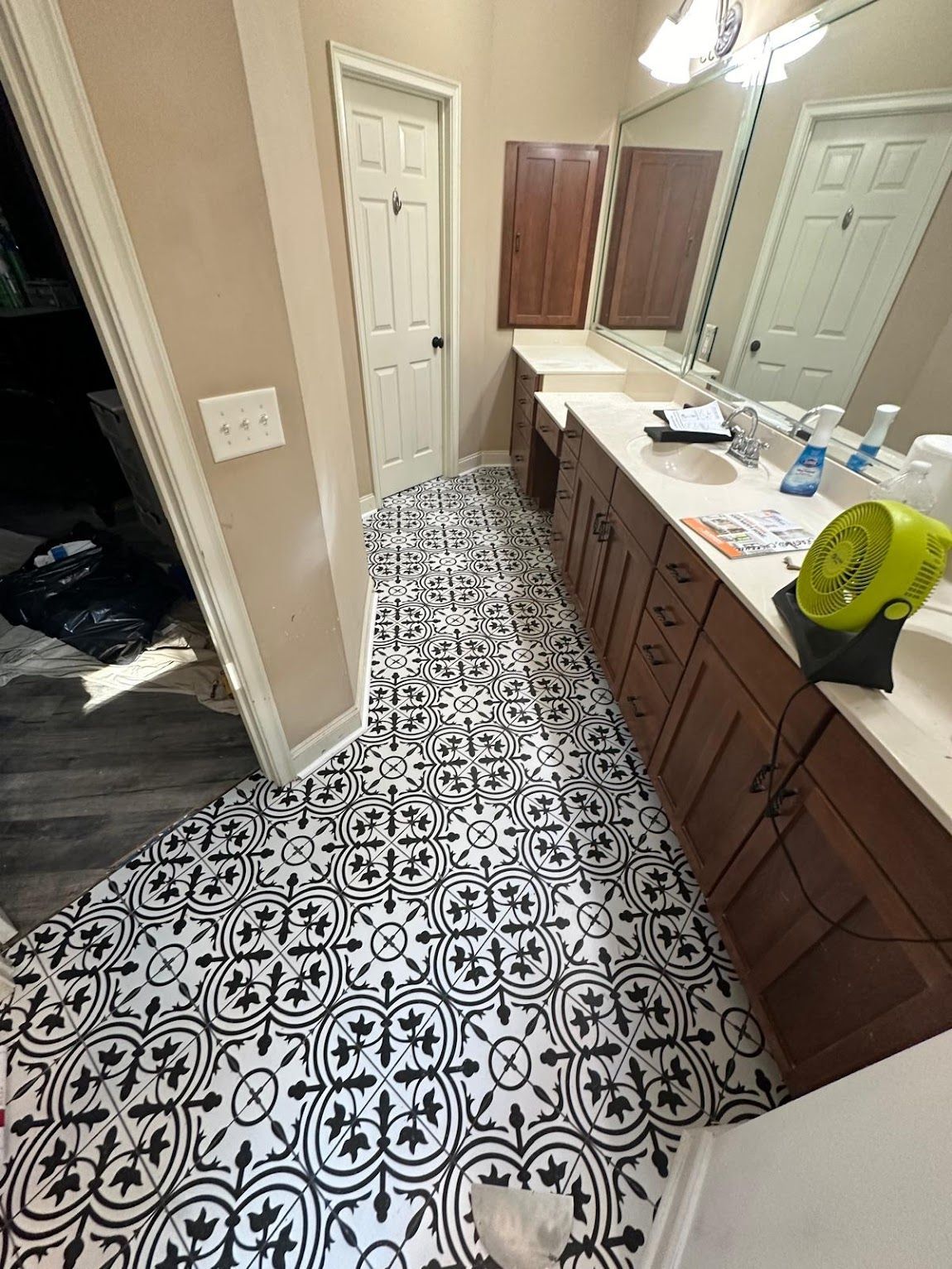 Bathroom with black and white patterned tile floor, wooden cabinets, and white countertops.