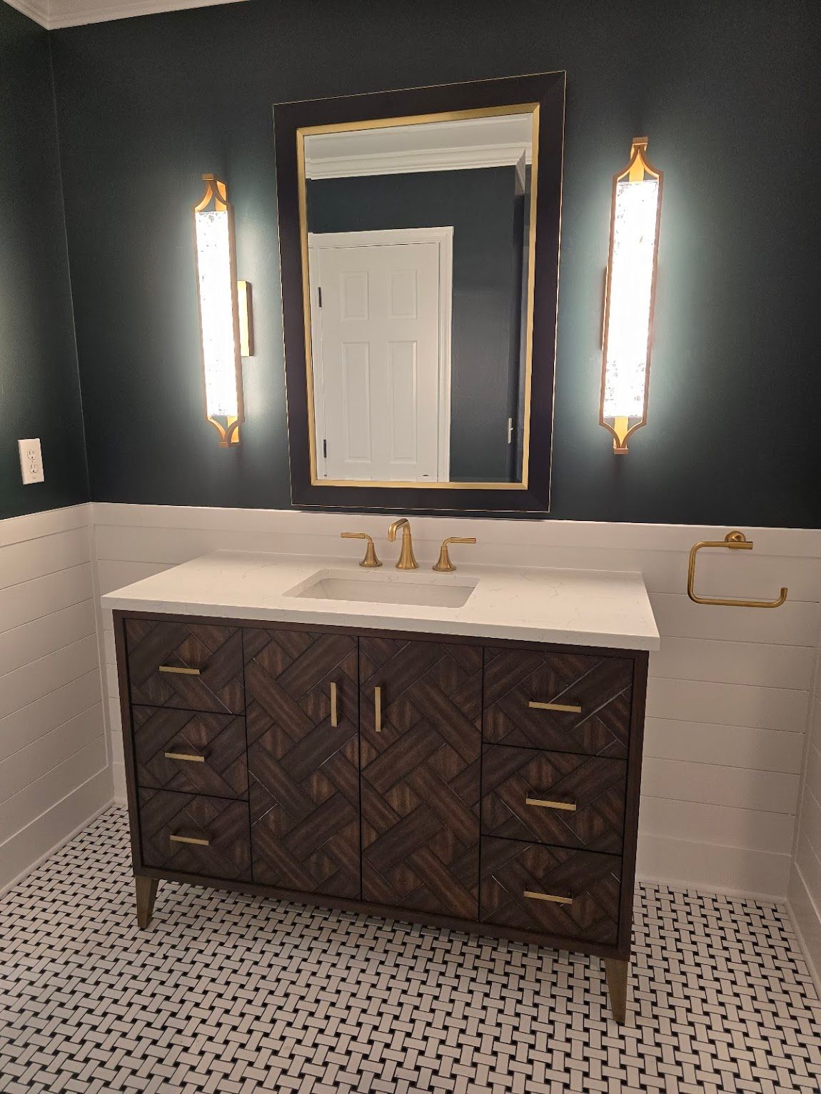 Bathroom with a dark patterned vanity, gold fixtures, and a large mirror flanked by sconces.
