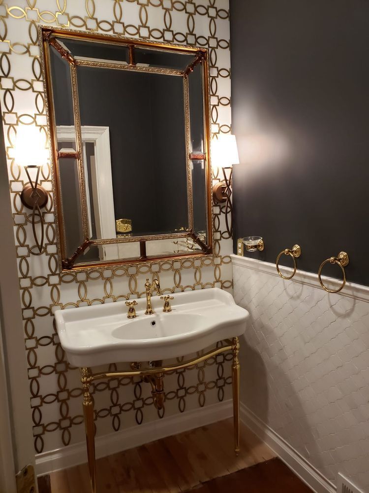 Elegant bathroom with gold accents: white sink, decorative wallpaper, ornate mirror, dark wall.