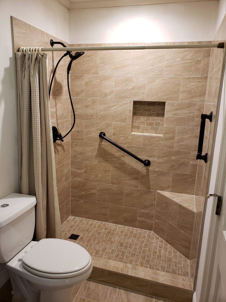 Shower stall with brown tiles, a built-in seat, grab bar, and a beige curtain.