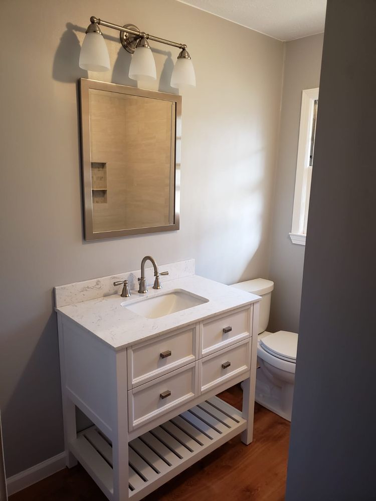 White vanity with drawers, a sink, and a mirror with a light fixture in a bathroom with neutral walls and a wooden floor.