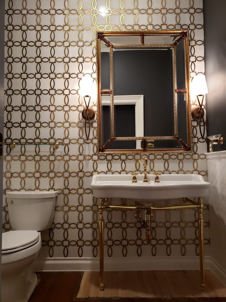 Gold-accented powder room with patterned wallpaper, gold mirror, sink, and fixtures.