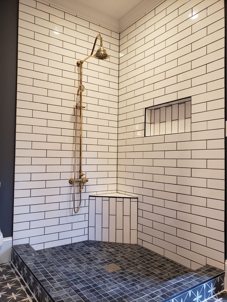 Shower stall with white subway tile, bronze fixtures, and dark mosaic floor.