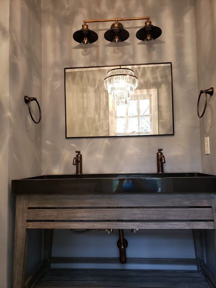 Bathroom vanity with a gray wooden cabinet, black countertop, double sinks, mirror, and bronze fixtures.