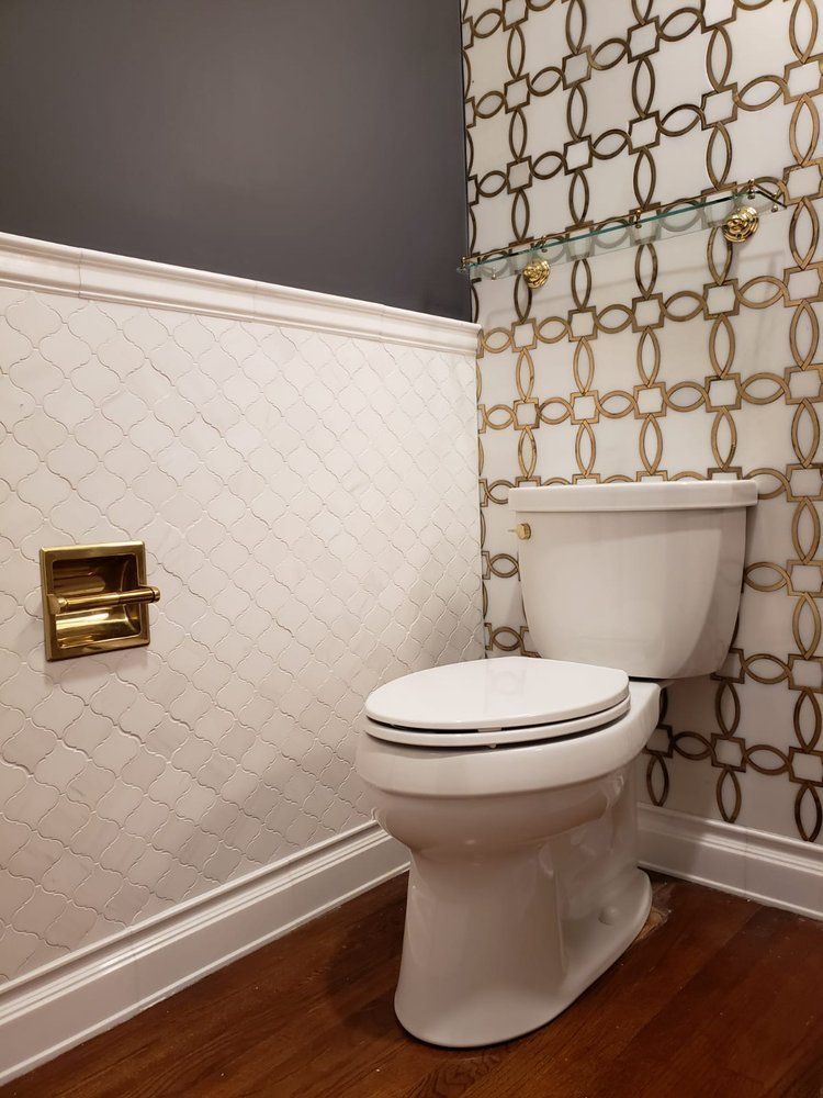 White toilet in a bathroom with patterned tile walls, dark wood floor, and gold accents.