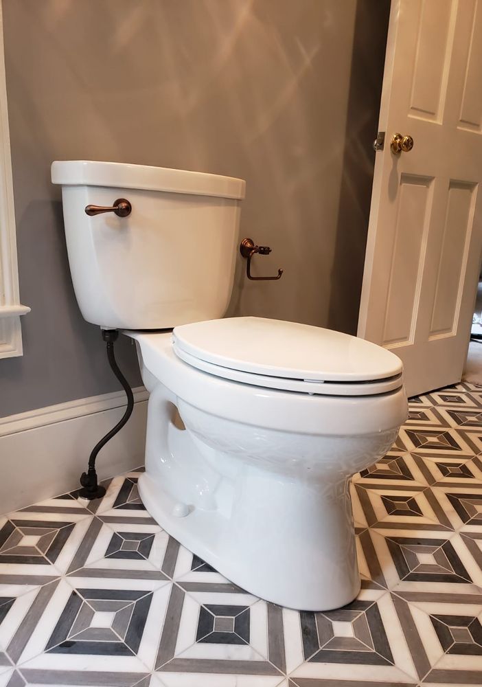 White toilet in a bathroom with gray walls, patterned tile floor, and a partially open white door.