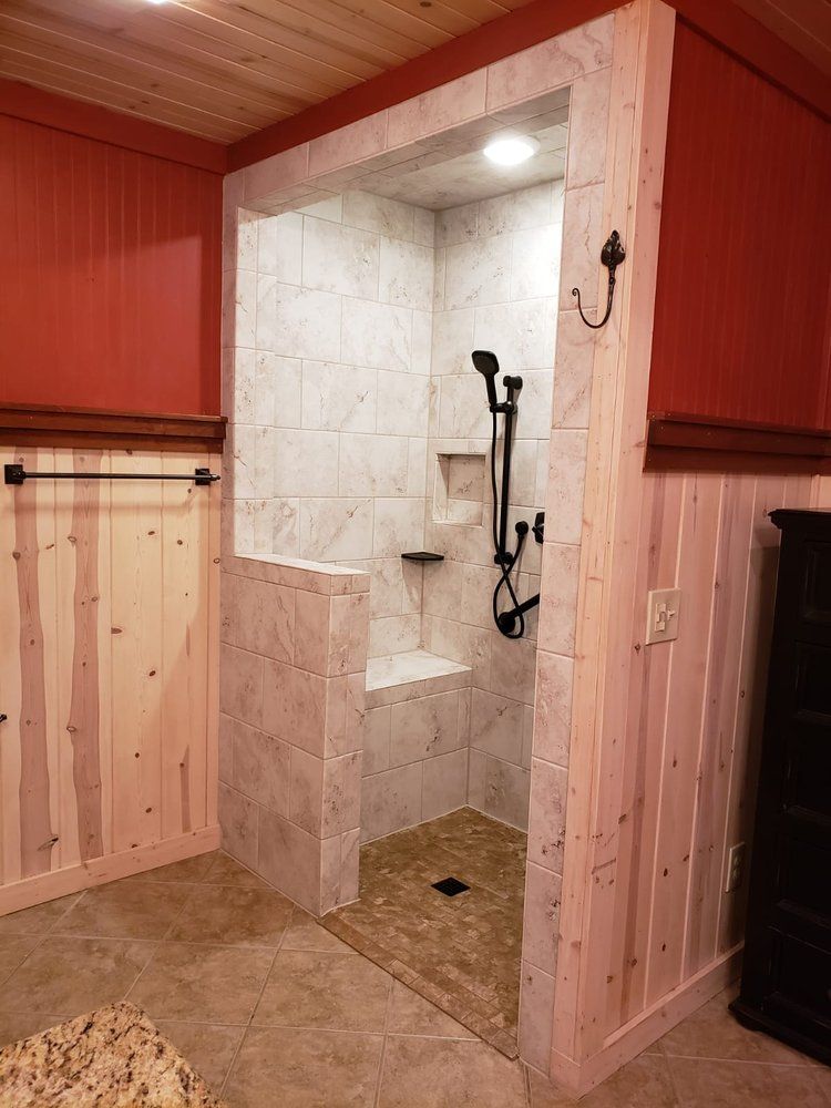 Walk-in shower with tiled walls and floor, stone bench, and black showerhead in a rustic-style bathroom.