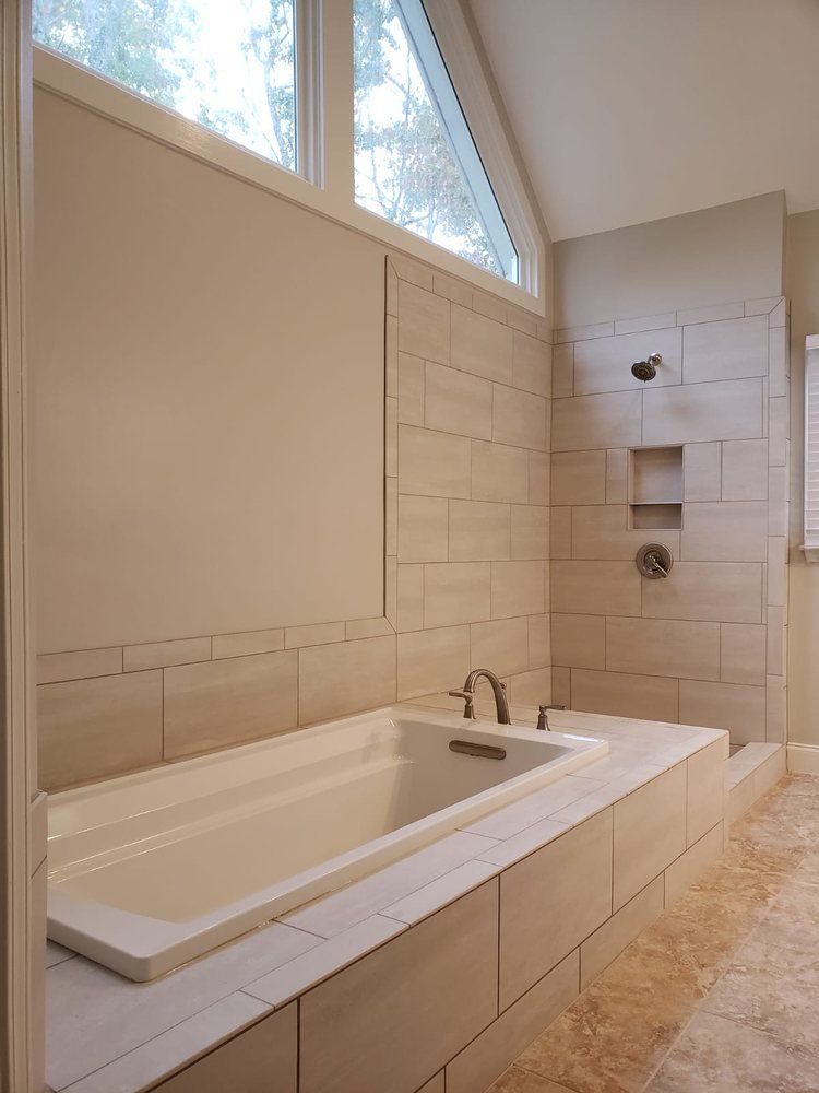 Modern bathroom with a bathtub, shower, and window. Beige tile walls and flooring.