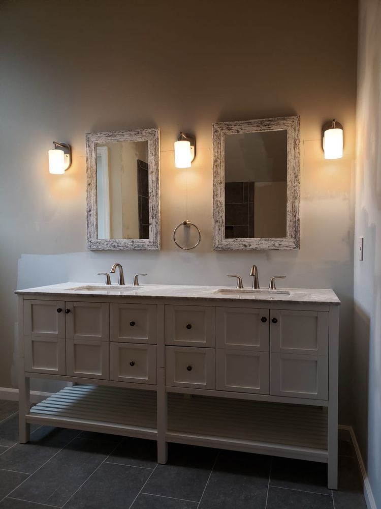 Double bathroom vanity with mirrors, sconces, and gray cabinet.