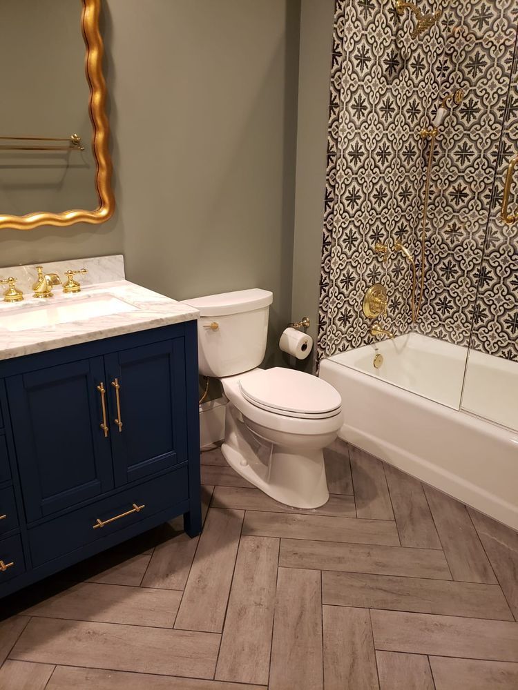 Navy blue vanity bathroom with gold accents, white toilet, patterned shower tile, and herringbone floor.