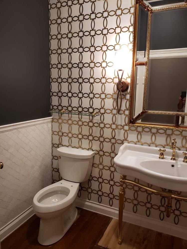 Powder room with gold and white patterned wallpaper, toilet, sink, mirror, and sconce.