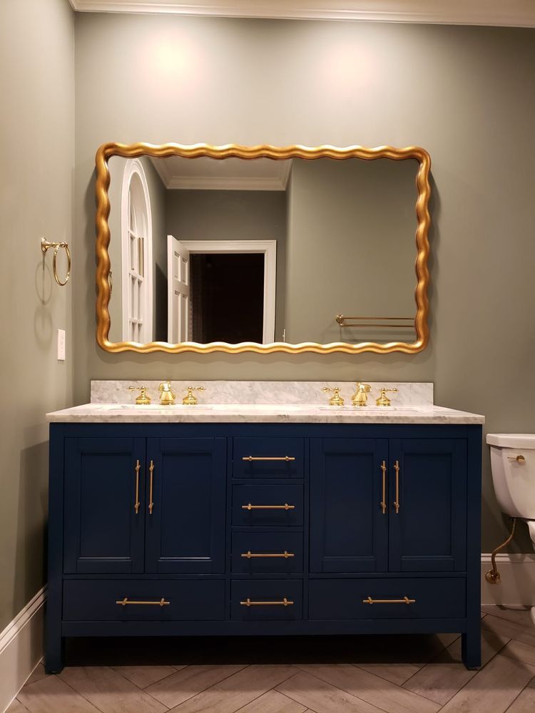 Blue bathroom vanity with gold hardware, marble countertop, gold-framed mirror, and light green walls.