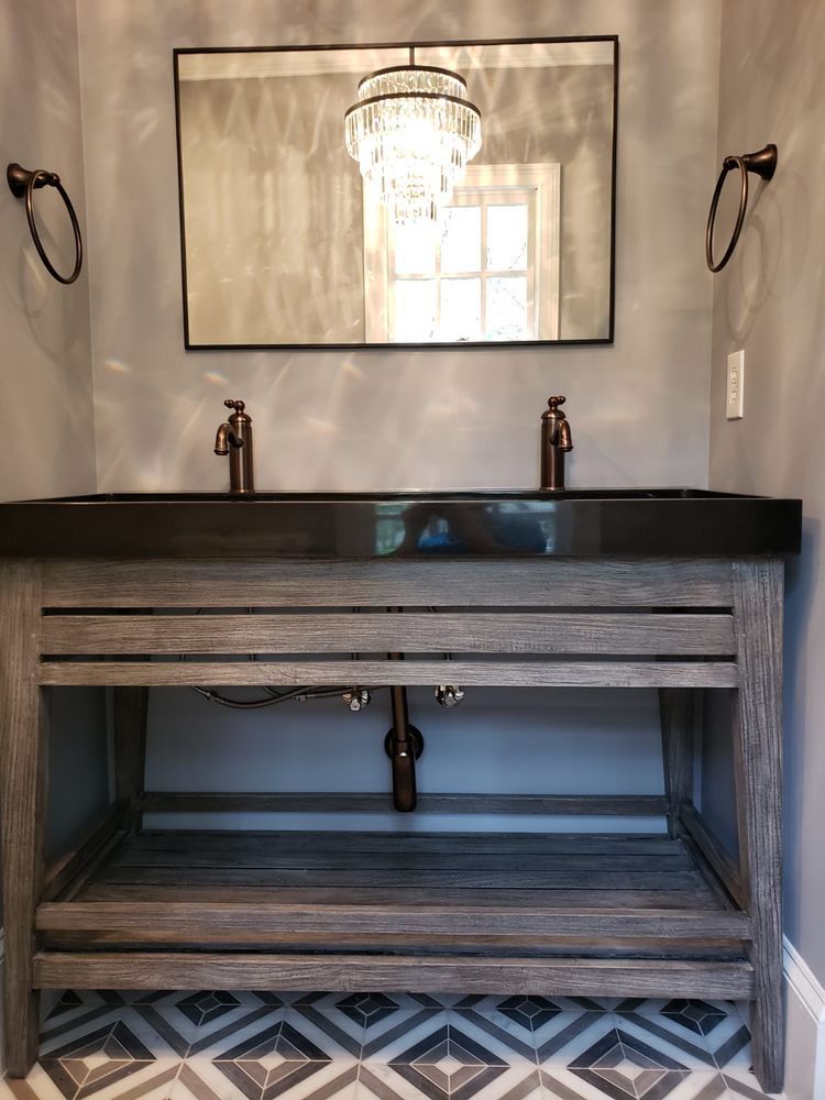 Double bathroom vanity with copper fixtures, gray wood cabinet, and black countertop. Decorative mirror, chandelier.