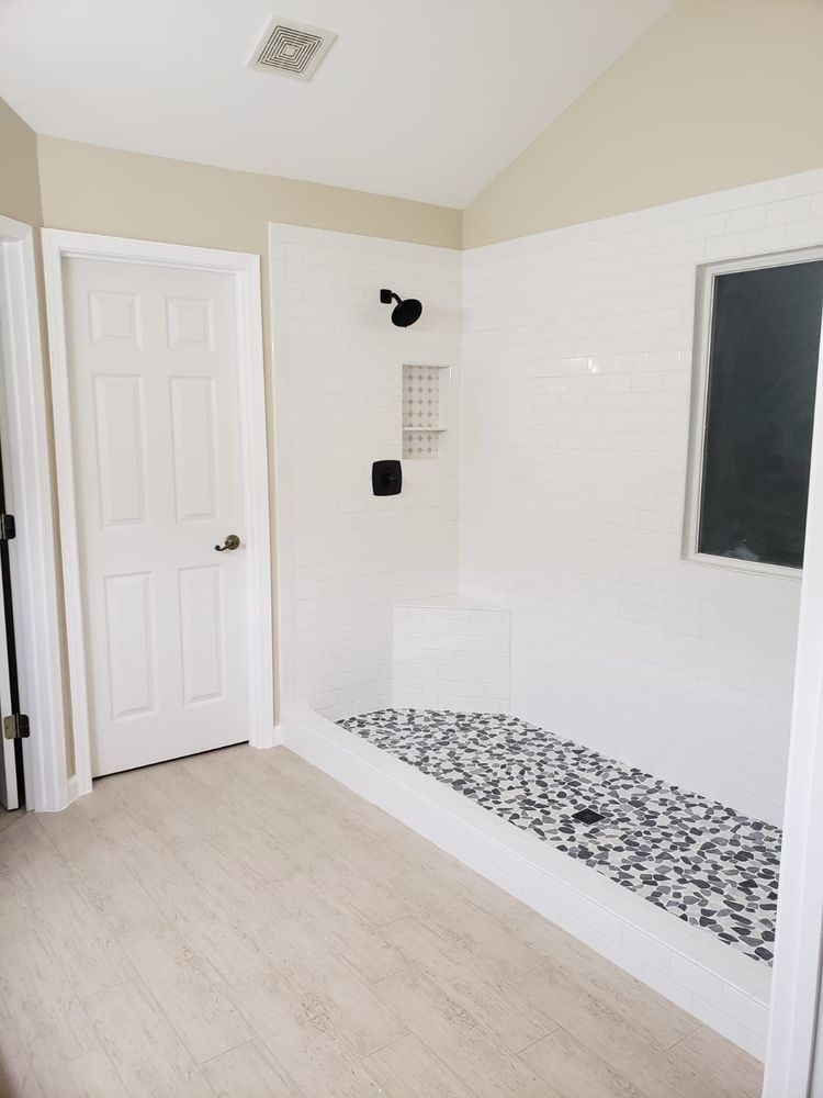 Modern bathroom with white walls, a black and white tiled shower floor, and a light wooden floor.