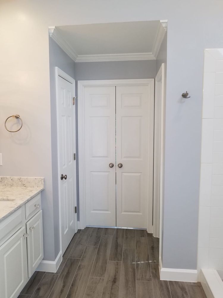 Bathroom entryway with double doors, gray walls, white trim, and wood-look tile flooring.