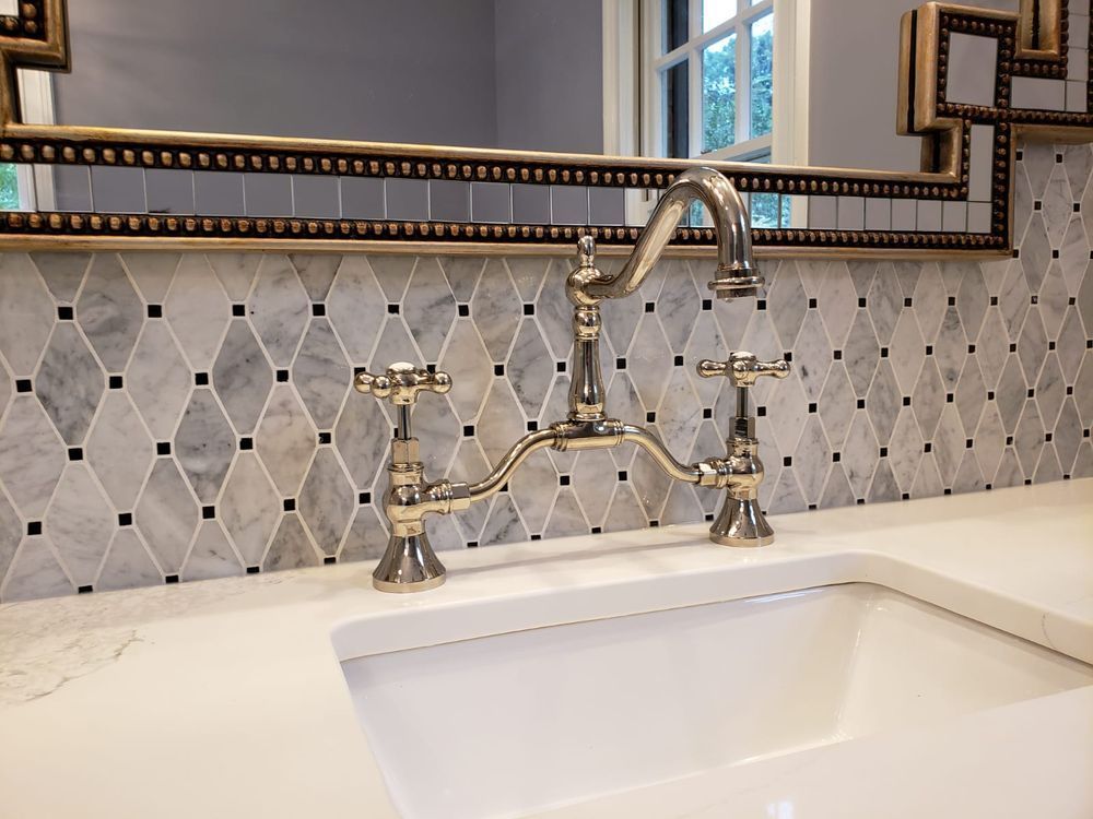 Bathroom sink with silver faucet, white countertop, and patterned tile backsplash.