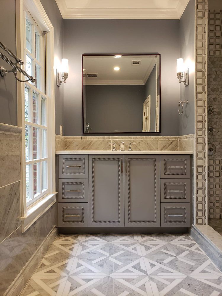 Bathroom with gray vanity, patterned floor, square mirror, sconces, and shower.