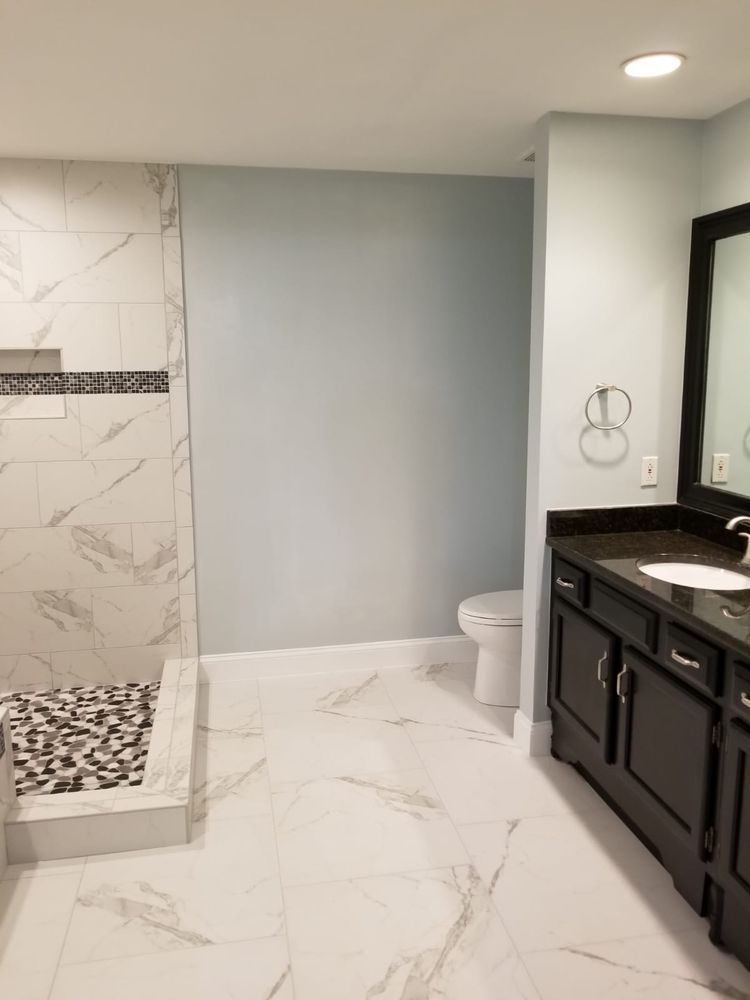 Bathroom with marble tile, a shower, toilet, dark cabinets, and light blue walls.
