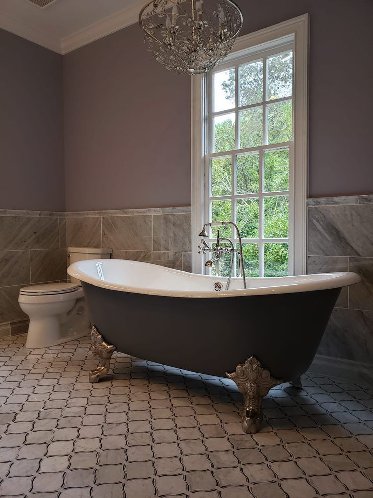 Bathroom with clawfoot bathtub, toilet, and window. Gray walls, marble tile, and ornate chandelier.