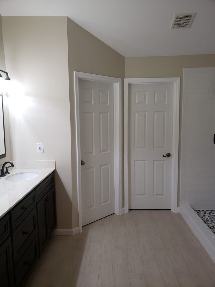 Bathroom with two white doors, dark vanity, and light-colored flooring.