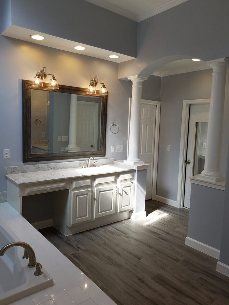 Bathroom with gray walls, white cabinets, marble countertop, large mirror, and decorative pillars.