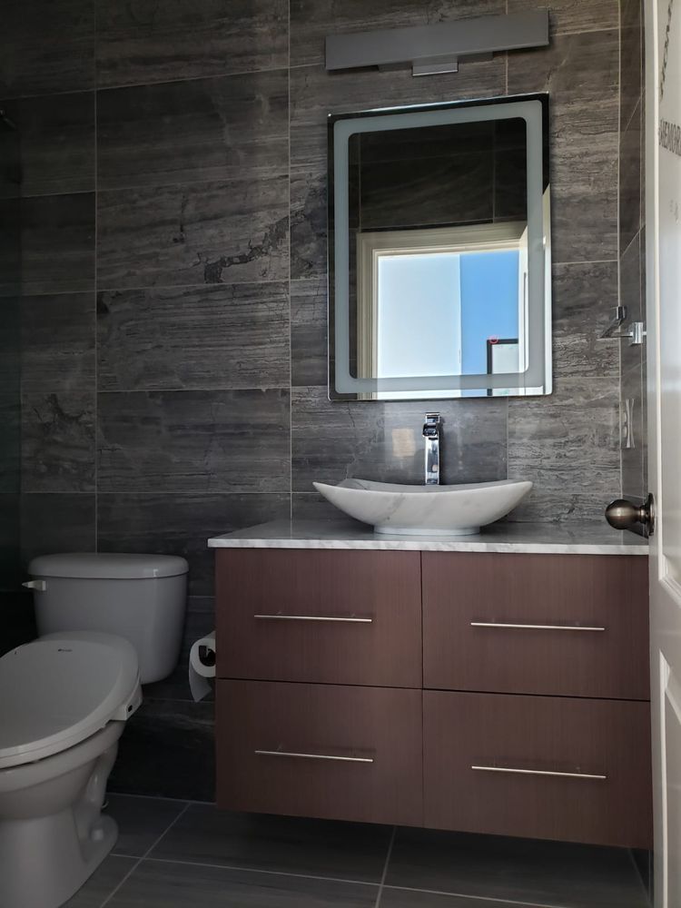 Modern bathroom with brown vanity, vessel sink, and gray tiled walls.