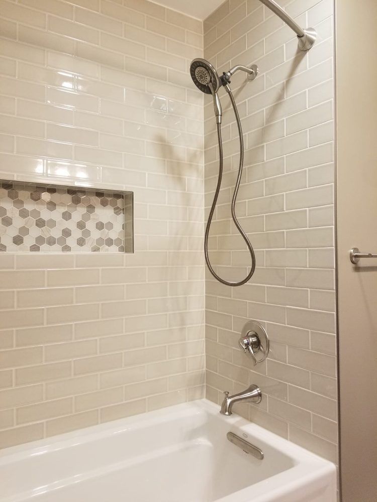 Shower with beige rectangular tiles, a niche with mosaic tiles, and a white bathtub.