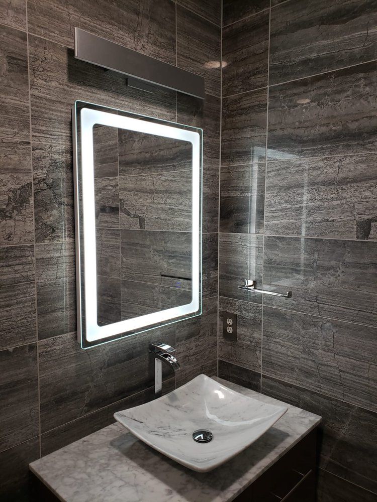 Modern bathroom with a lighted mirror, vessel sink, and gray tiled walls.